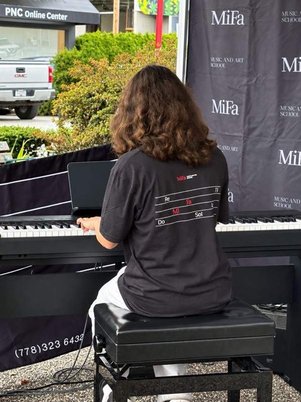 Student playing piano in a MiFa T-shirt, viewed from behind